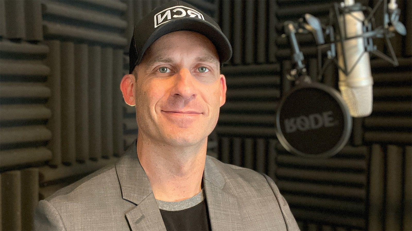 Phil Ellering stands in a podcast recording booth. He is wearing a black baseball cap with an RCN logo.