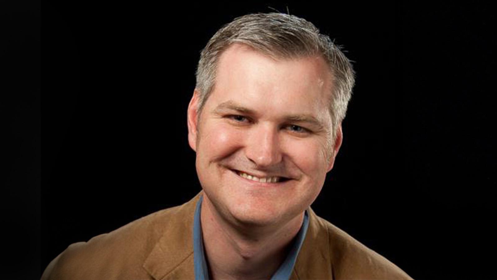 Eric Rosenfeld smiles at the camera. He has gray hair and is wearing a blue collared shirt with a tan blazer.