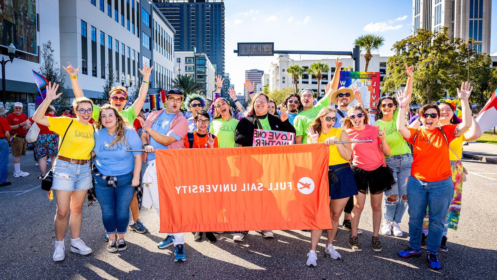 A group of Full Sail faculty, students, and staff posing with a large orange banner that reads “Full Sail University”