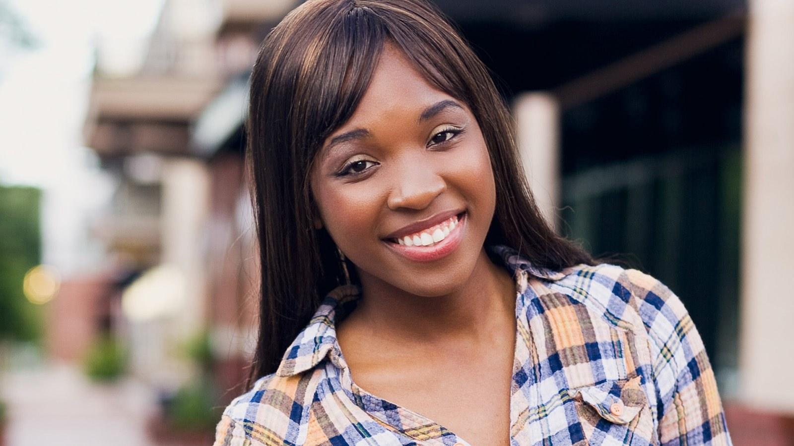 Brandie Green smiles at the camera. She is standing outdoors and wearing a flannel button-down shirt.