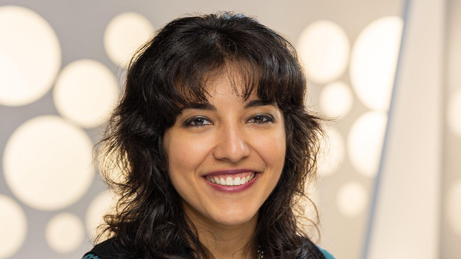 A headshot of a woman with a dark brown shag haircut smiling against a white background.