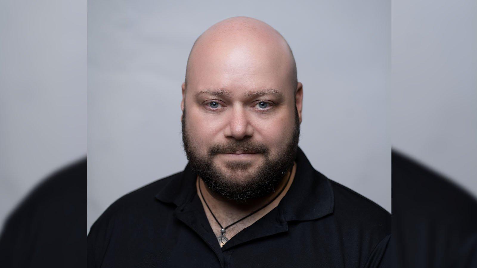 Grad Corey Guerra is wearing a black polo shirt and posing for a headshot against a light grey backdrop.