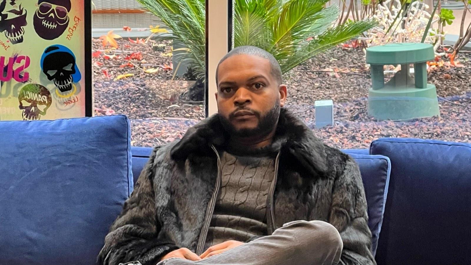 Terique Walker sits on a blue sofa wearing a black fur coat and turtleneck.