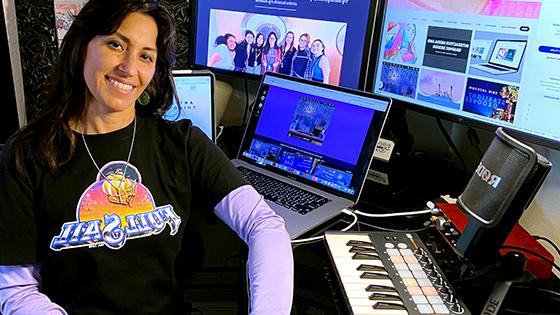 Instructor Milena Jackson, a woman with shoulder-length dark hair, is seated at her desk while wearing a Full Sail University graphic tee.