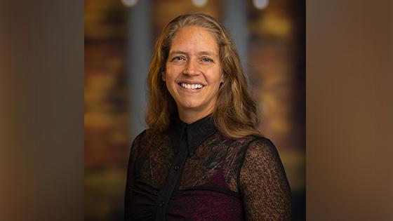 Phoebe Elefante, a woman with shoulder-length light brown hair and a black blouse smiling in front of an out-of-focus brown backdrop.