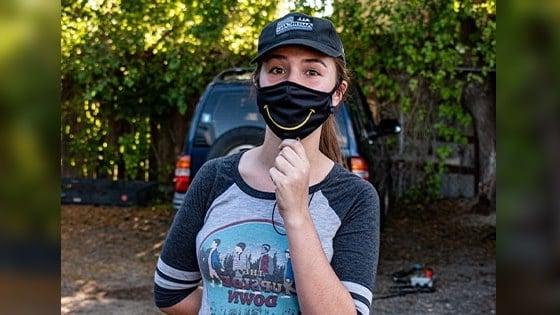 Paola Beck Gisler stands wearing a black mask with a yellow smile.