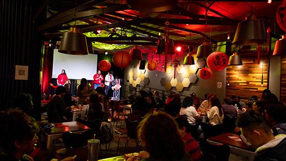 A group gathered at Full Sail's Treehouse, guests sitting down and the hosts on stage. The room is dimly lit and decorated with red paper lanterns for the Lunar New Year.