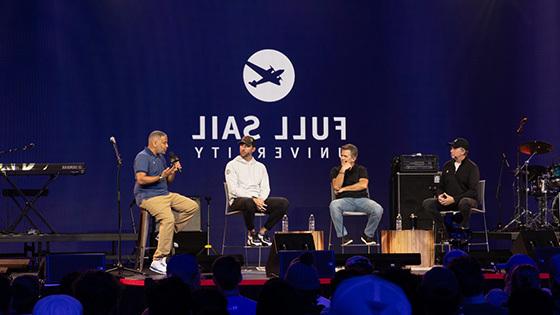 MLB Pitcher Adam Wainwright and three other people are seated on a stage during a panel, the large-scale LED screen behind them reads “Full Sail University” against a blue backdrop.