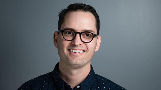 Digital Arts & Design grad Paul Shank wearing a blue, polka-dotted shirt in front of a gray background.