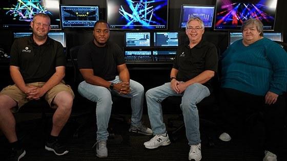 Four people sitting in front of a Grand MA lighting console at Full Sail University.