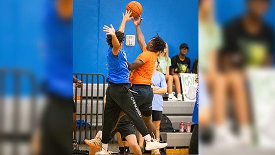 Two basketball players jump up simultaneously to reach the basketball on a court. They are both wearing athletic clothing.