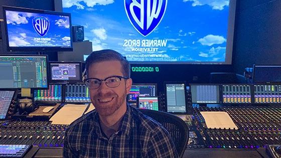 记录 艺术s grad Ryan Kennedy sits in front of a large recording console.