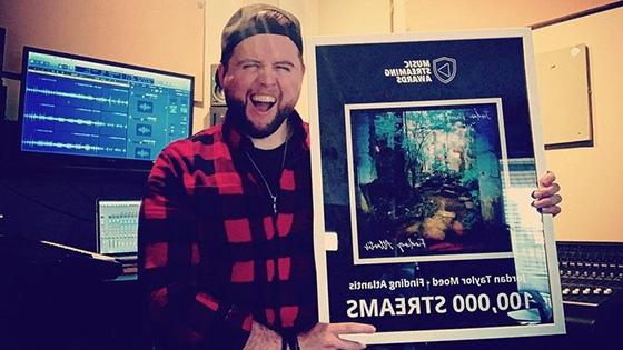 Jordan Moed stands in his studio and holds an award for 10,000 streams for his song “Finding Atlantis.”