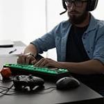 A man wearing a gaming headset sits at a desk with a gaming keyboard, an Xbox controller, 和一个地下城 & 龙死.