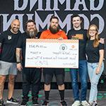 Sam Lupo, DrLupo, Bennett Newsome, and Kevin Murray on stage in the Fortress with a student in an orange Armada jersey receiving an oversized scholarship check.