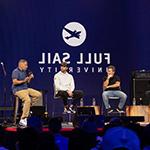 MLB Pitcher Adam Wainwright and three other people are seated on a stage during a panel, the large-scale LED screen behind them reads “满帆大学” against a blue backdrop.