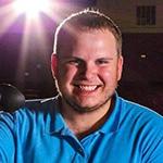 Grad Cody Grammer in a blue collared shirt, holding a video camera in a movie theater.