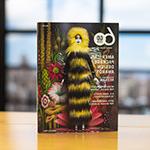 Graphic 设计 USA’s April 2023 issue sits upright on a wooden table. The cover features a female doll wearing a long furry black-and-yellow dress with a hood. She is standing in front of a psychedelic floral background.