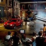 Full Sail University's Backlot in the evening filled with a full film production crew shooting a scene featuring two muscle cars, one red and one black.