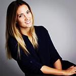 Grad Lisa Maskey, a smiling woman with straight blond hair wearing a black three-quarter sleeve top seated against a grey backdrop.