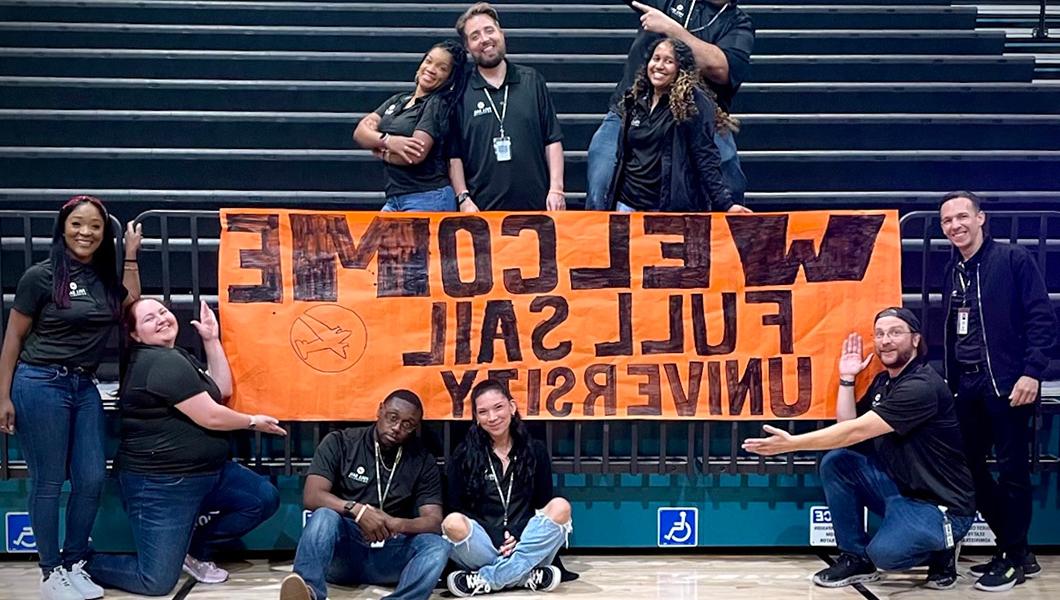 满帆 staff members posing for a photo with an orange handmade sign that reads “Welcome 满帆大学.”